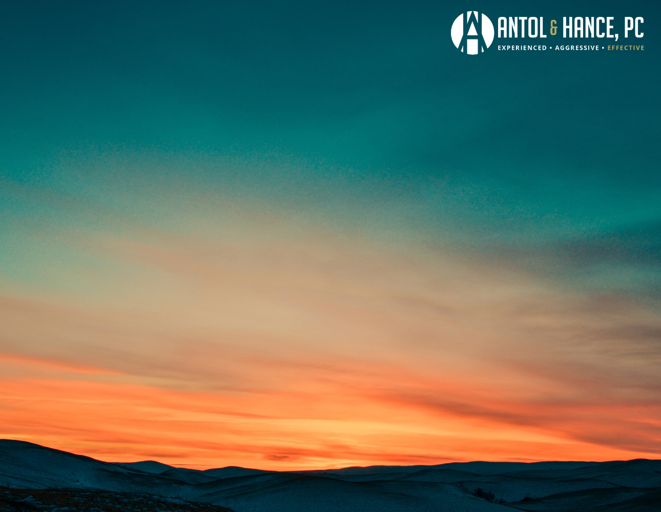 Image shoes a photograph of a rising sun coming up over the horizon through a layer of clouds, slowly illuminating a mountain range of snowy peaks below.